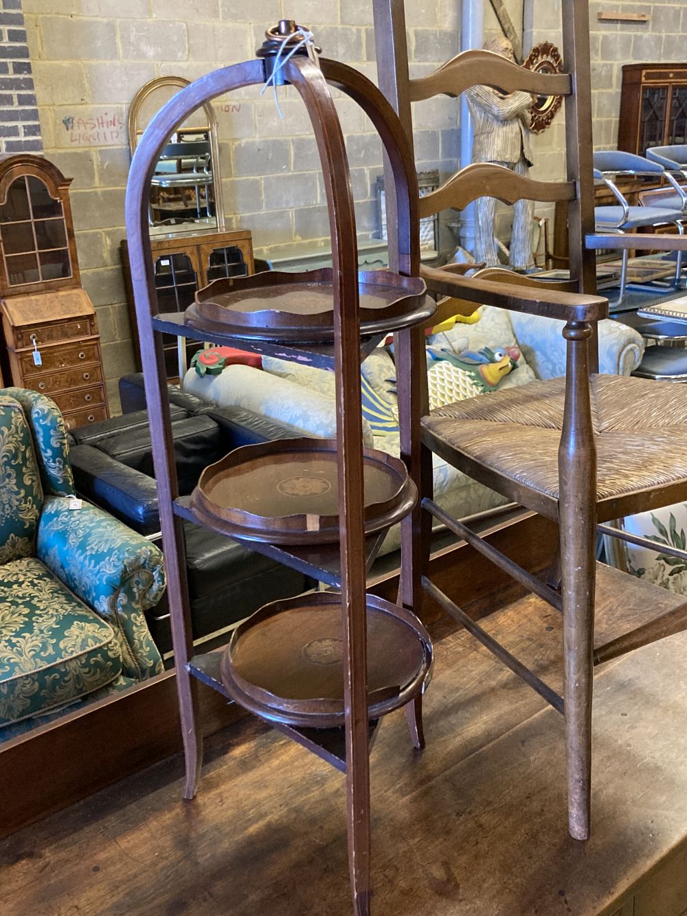 An Arts & Crafts ladder-back rush-seat elbow chair and an Edwardian inlaid mahogany three-tier cake stand (faults), 96cm high